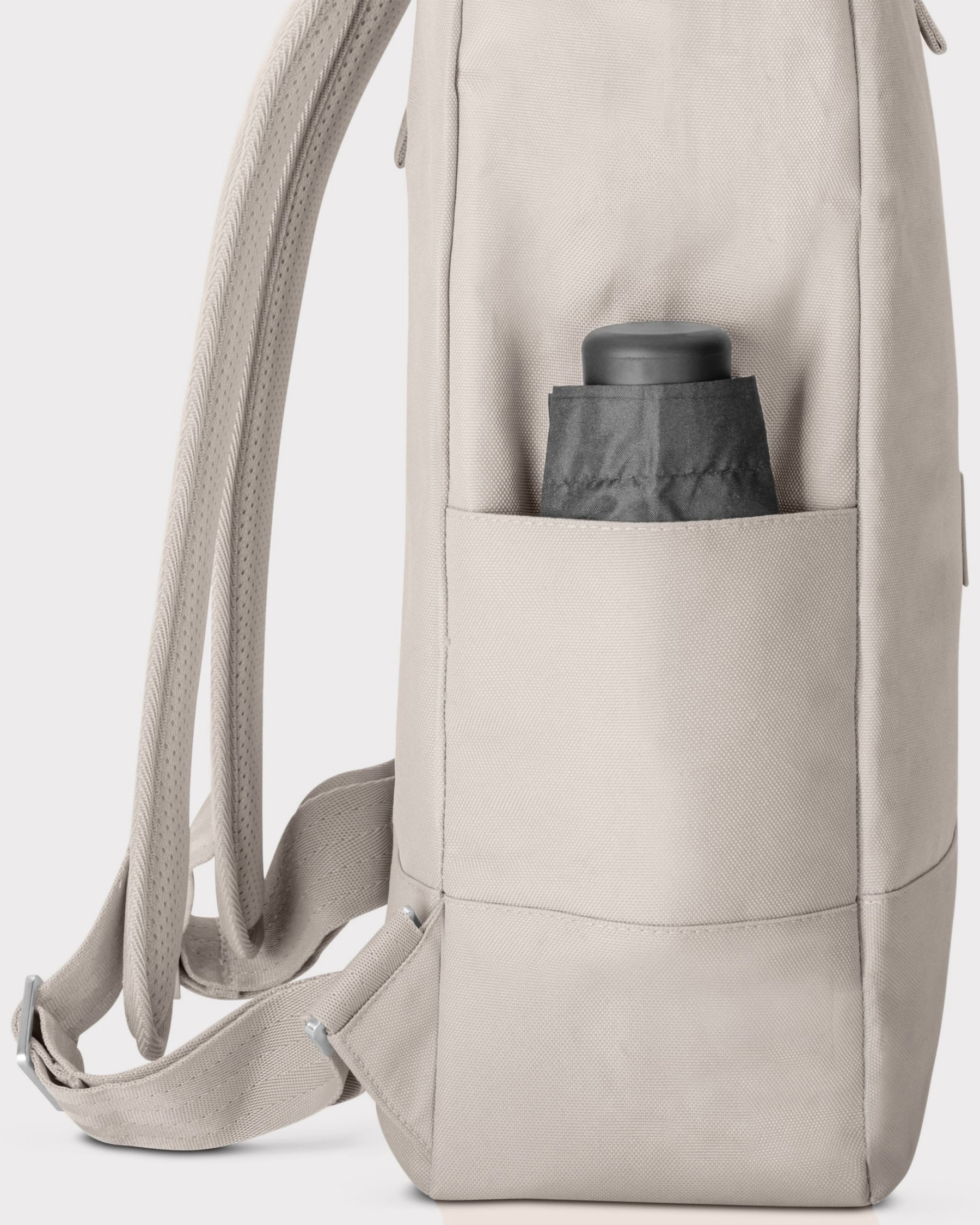 Seitenansicht des hellgrauen Rolltop Rucksacks 'Robin Large' mit einer seitlichen Tasche und einem schwarzen, eingesteckten Gegenstand