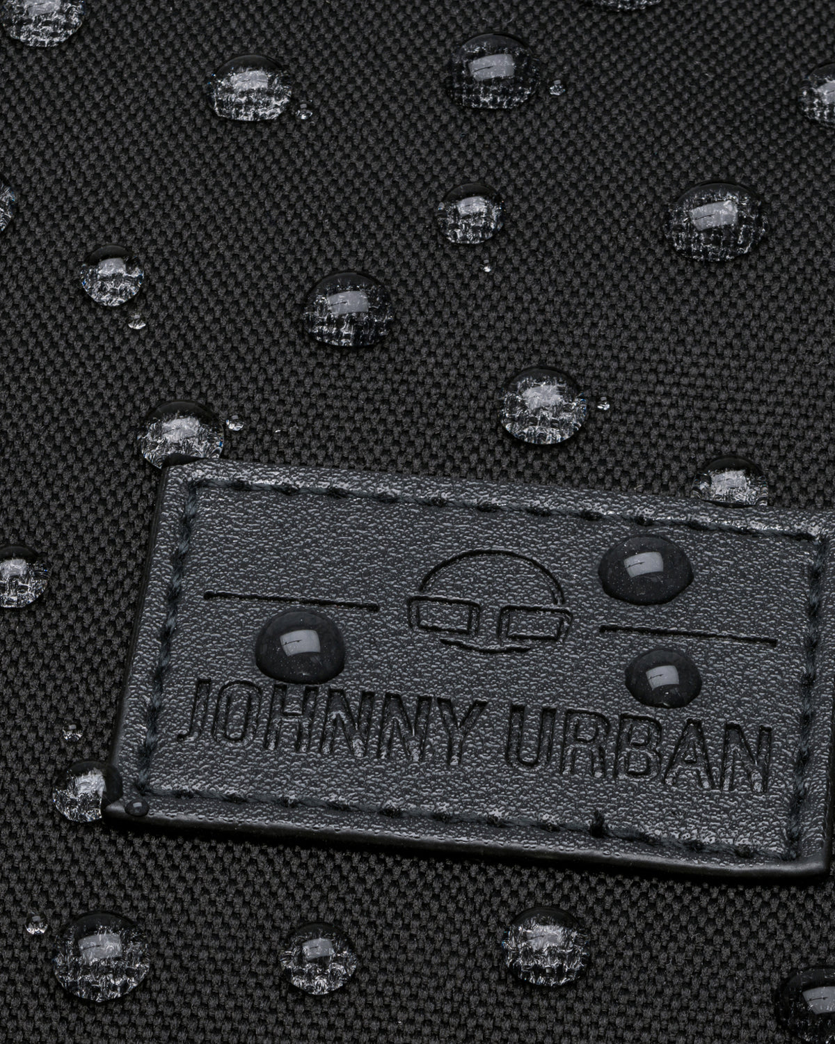 Nahaufnahme eines Gewebematerials mit Johnny Urban Logo und wasserabweisenden Wassertropfen darauf