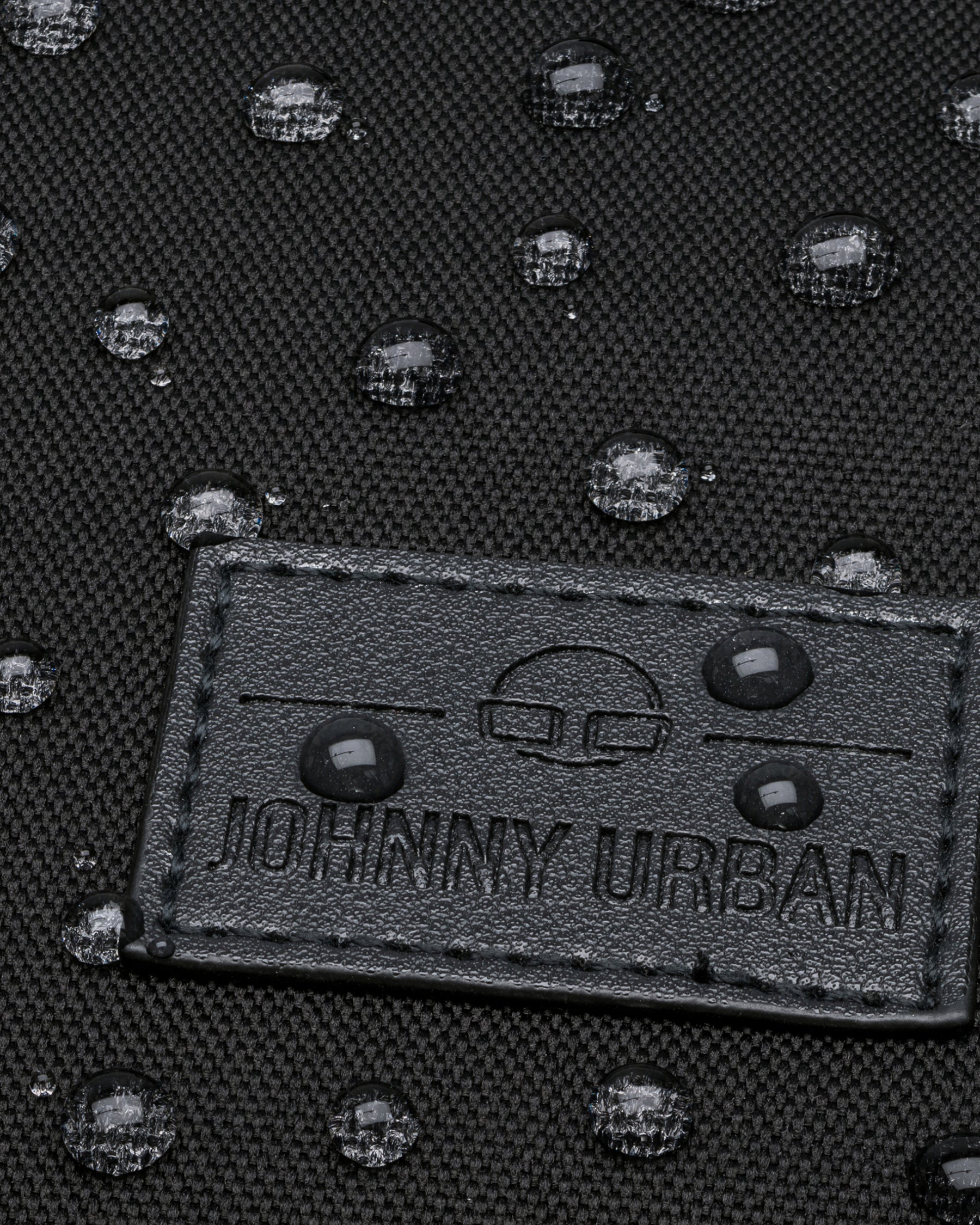 Nahaufnahme eines Gewebematerials mit Johnny Urban Logo und wasserabweisenden Wassertropfen darauf
