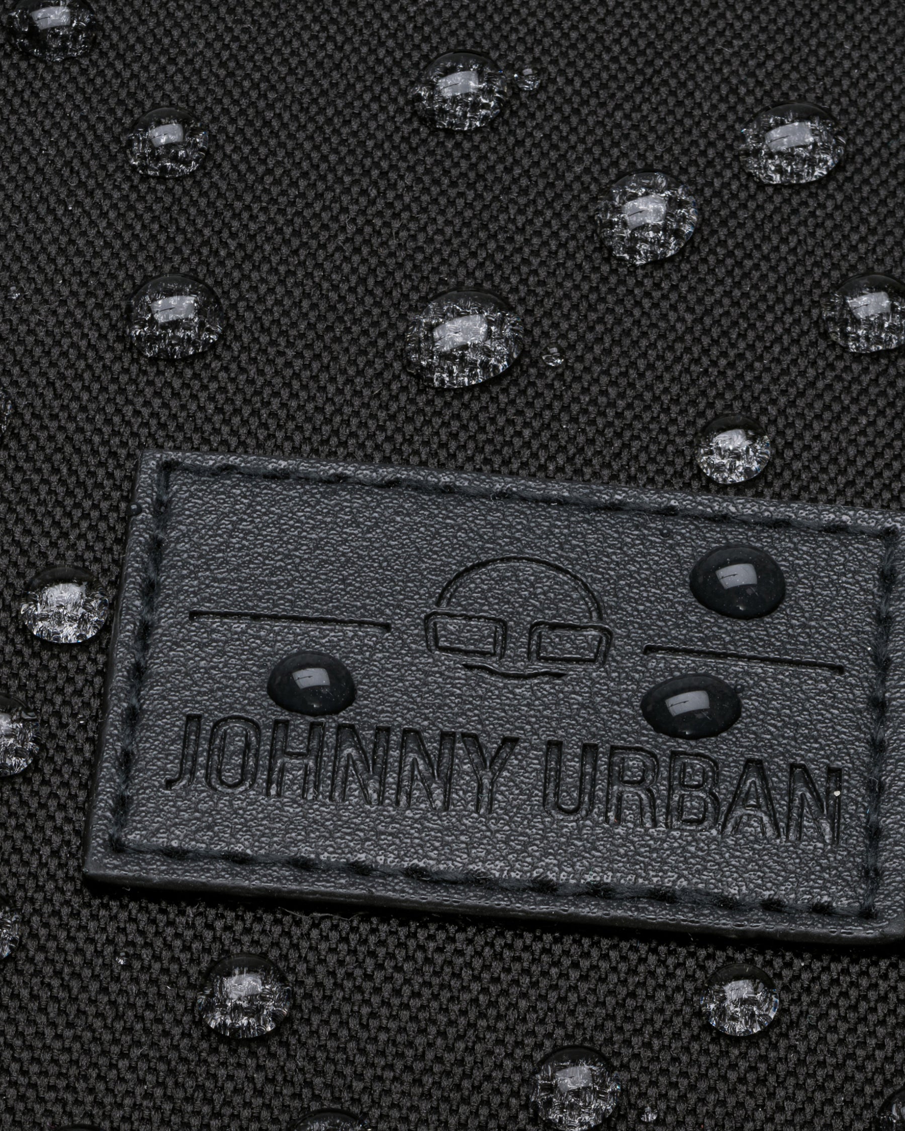 Nahaufnahme des schwarzen Johnny Urban Logos auf einem wasserabweisenden Rolltop-Rucksack 'Robin Medium' mit Wassertropfen