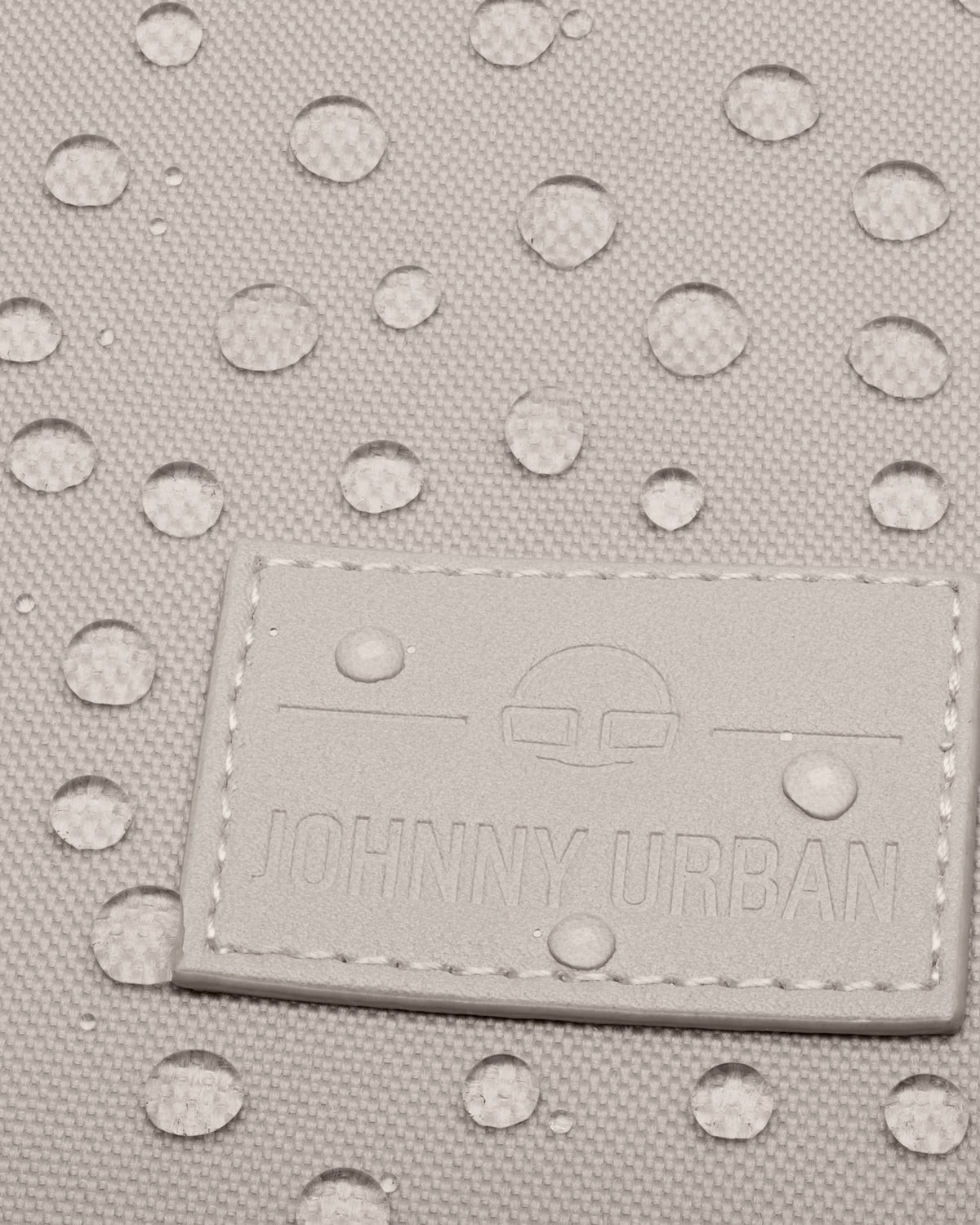 Nahaufnahme des Johnny Urban Logos auf einem wasserabweisenden Rolltop Rucksack Stoff mit Wassertropfen