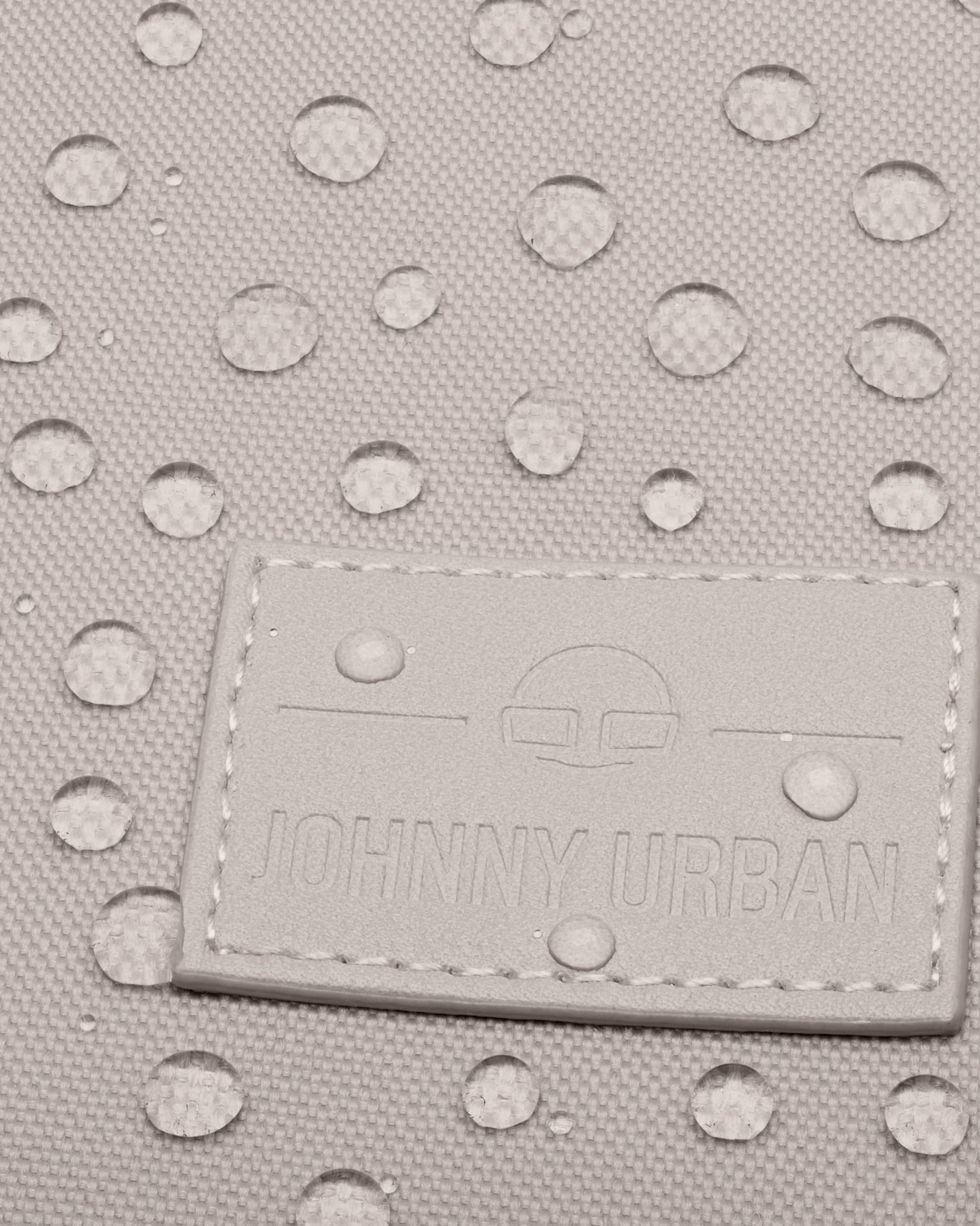 Nahaufnahme des Johnny Urban Logos auf einem wasserabweisenden Rolltop Rucksack Stoff mit Wassertropfen