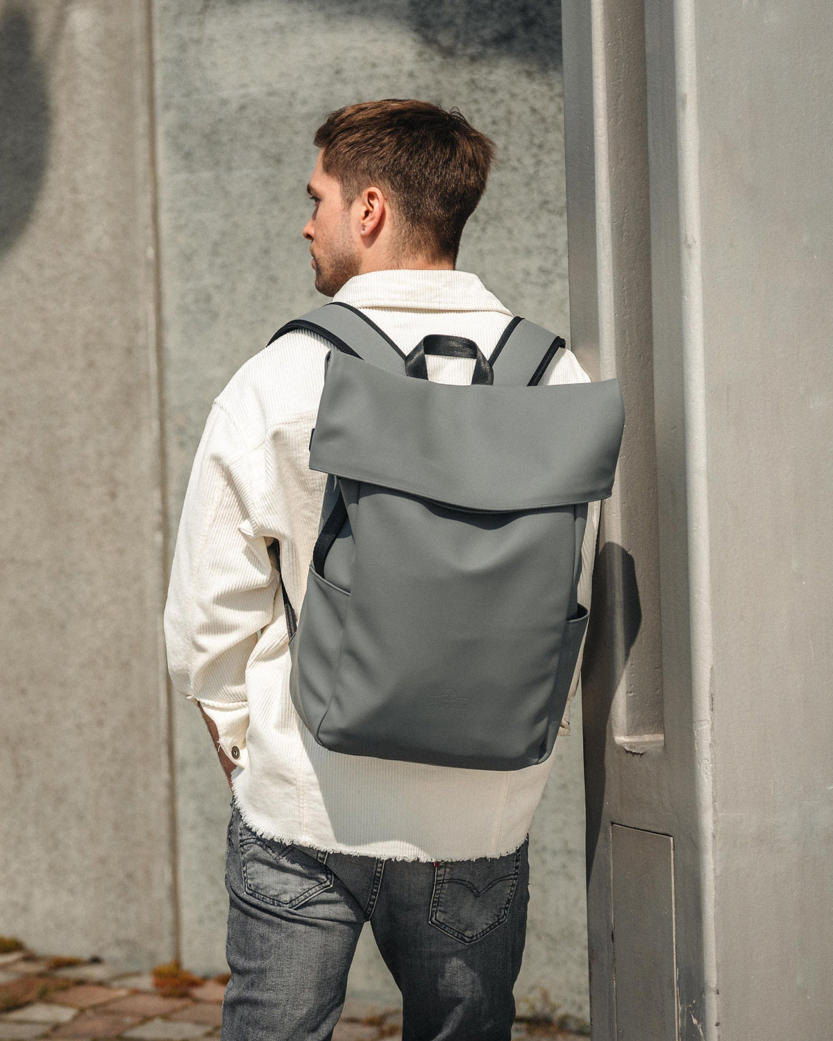 Mann trägt grauen Rolltop Rucksack 'Henry' von Johnny Urban mit weißem Hemd und grauer Jeans