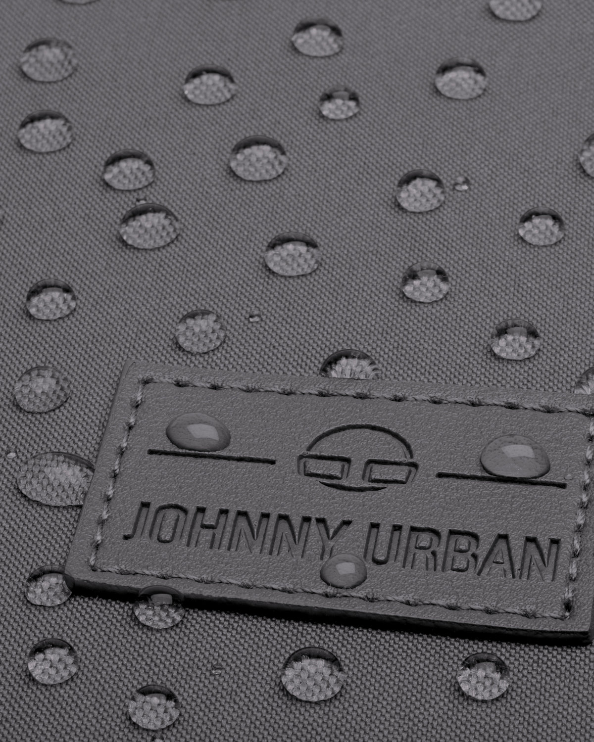 Detailaufnahme des wasserabweisenden grauen Gewebes und des Johnny Urban Logos auf dem Rucksack Jona Large