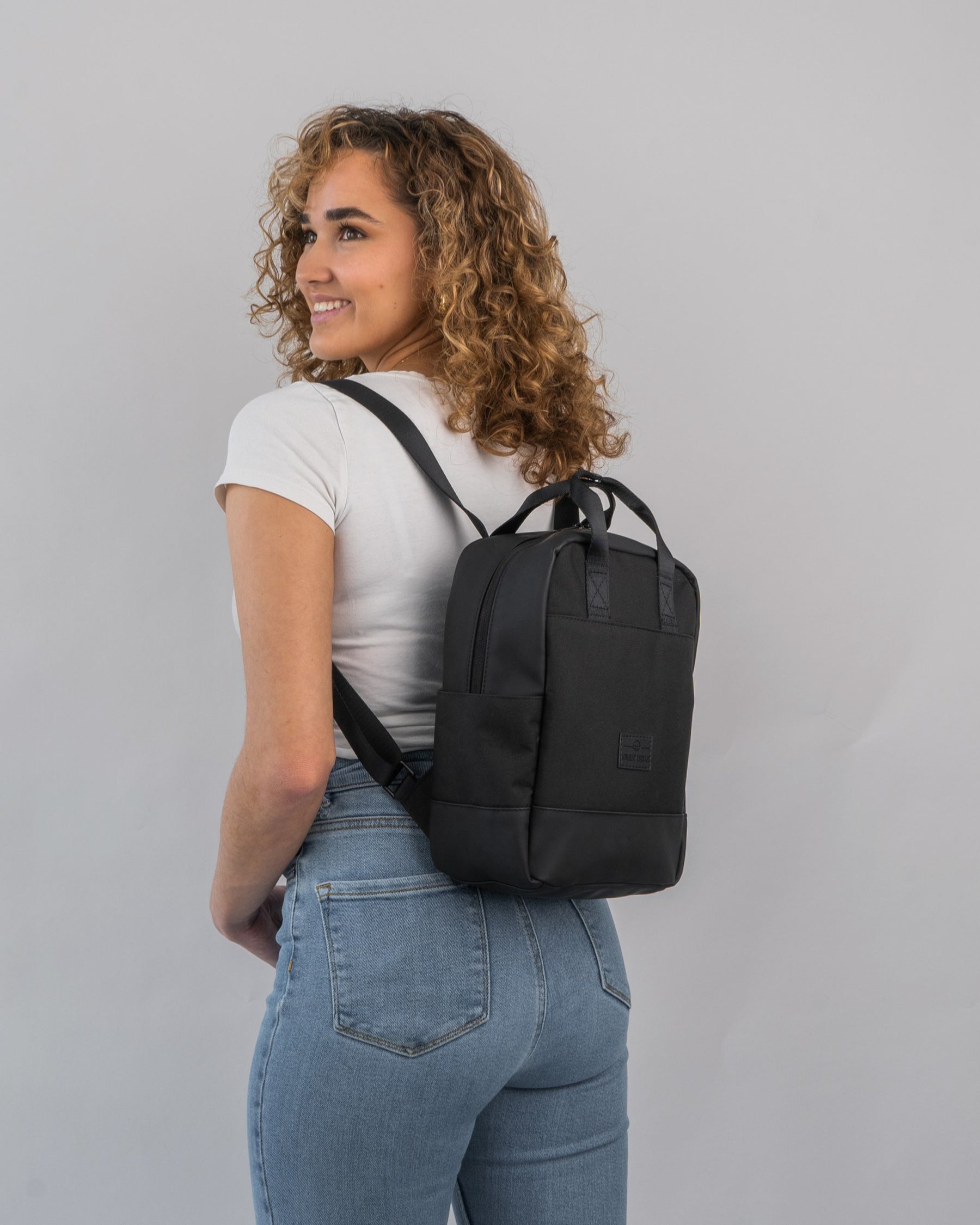 Frau mit lockigem Haar trägt schwarzen kleinen Rucksack 'Jona Small' von Johnny Urban