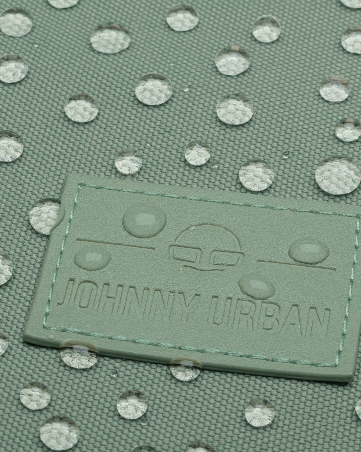 Nahaufnahme der wasserabweisenden Oberfläche und Markenprägung des Rucksacks 'Jona Small' von Johnny Urban