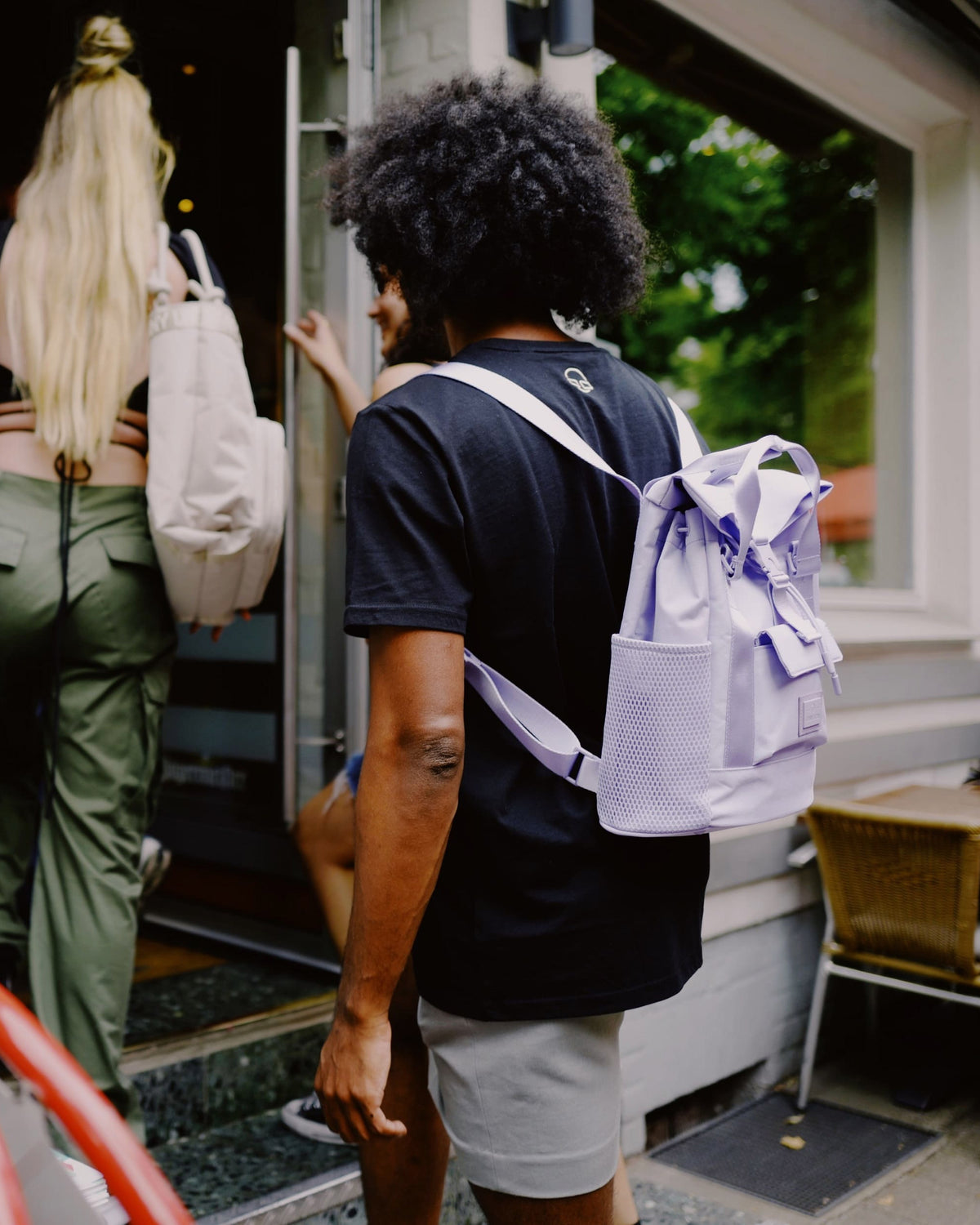 Person mit schwarzem T-Shirt trägt lila Rucksack 'Jules' von Johnny Urban, andere Personen gehen voran in ein Gebäude