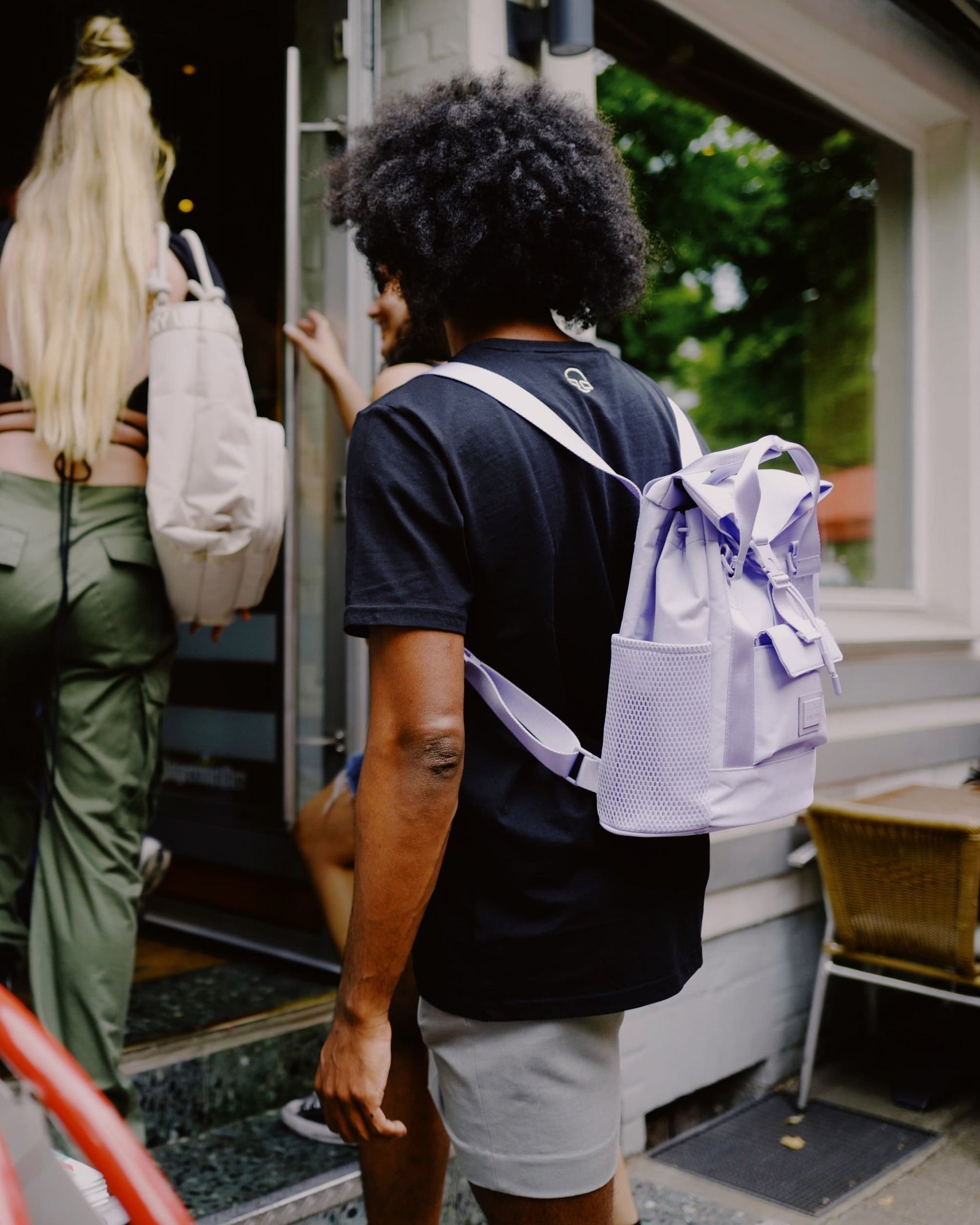 Person mit schwarzem T-Shirt trägt lila Rucksack 'Jules' von Johnny Urban, andere Personen gehen voran in ein Gebäude