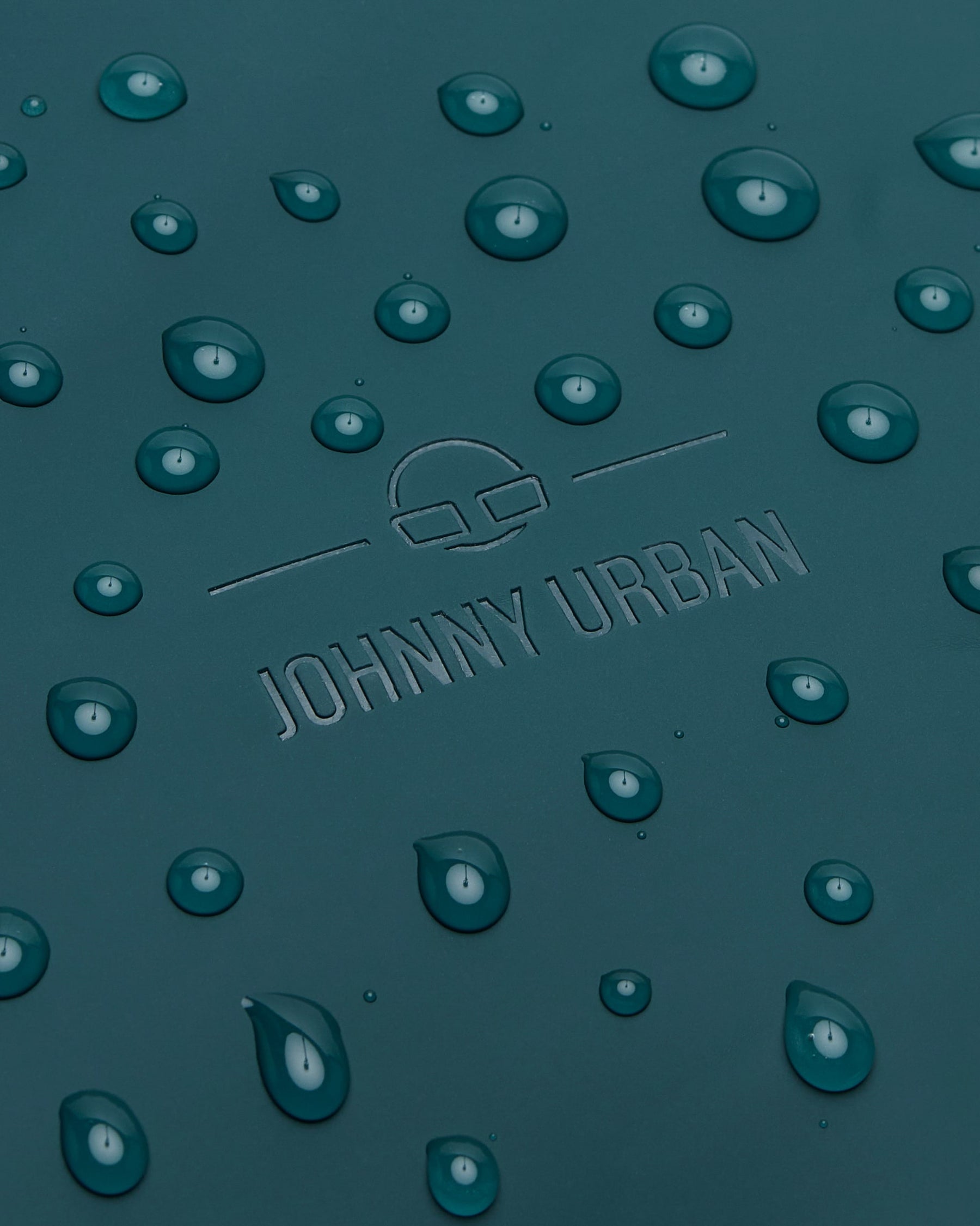 Nahaufnahme des petrolfarbenen Johnny Urban Rolltop Rucksacks 'Henry' mit Wasserperlen auf der Oberfläche
