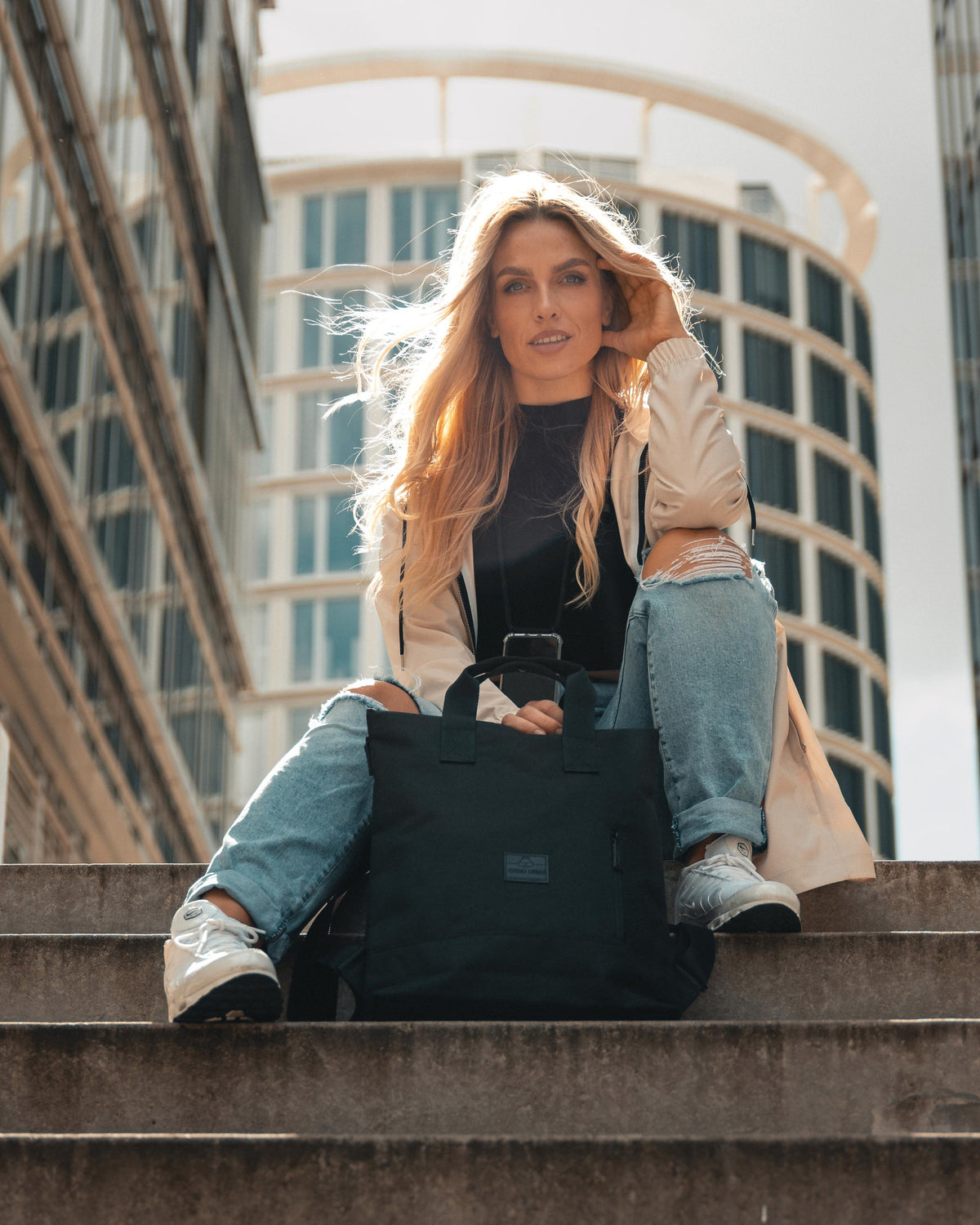 Frau sitzt auf Treppe in Stadt mit schwarzem Johnny Urban Rucksack 'Ivy' auf dem Boden