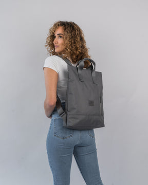 Frau mit lockigem Haar trägt dunkelgrauen Rucksacktasche 'Ivy' von Johnny Urban über weißen T-Shirt und Jeans