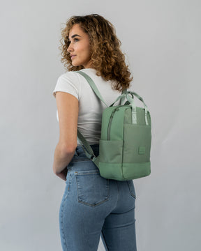 Frau mit lockigem Haar, die den kleinen, nachhaltigen Jona Small Rucksack in grün trägt