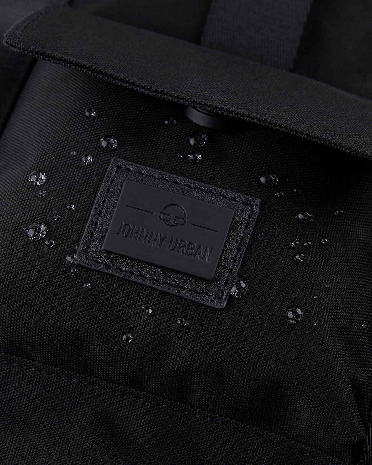 Nahaufnahme des schwarzen wasserabweisenden Rucksacks 'Jules' mit Johnny Urban Logo und Wassertröpfchen auf dem Stoff