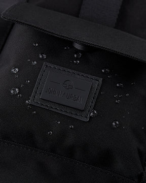Nahaufnahme des schwarzen wasserabweisenden Rucksacks 'Jules' mit Johnny Urban Logo und Wassertröpfchen auf dem Stoff